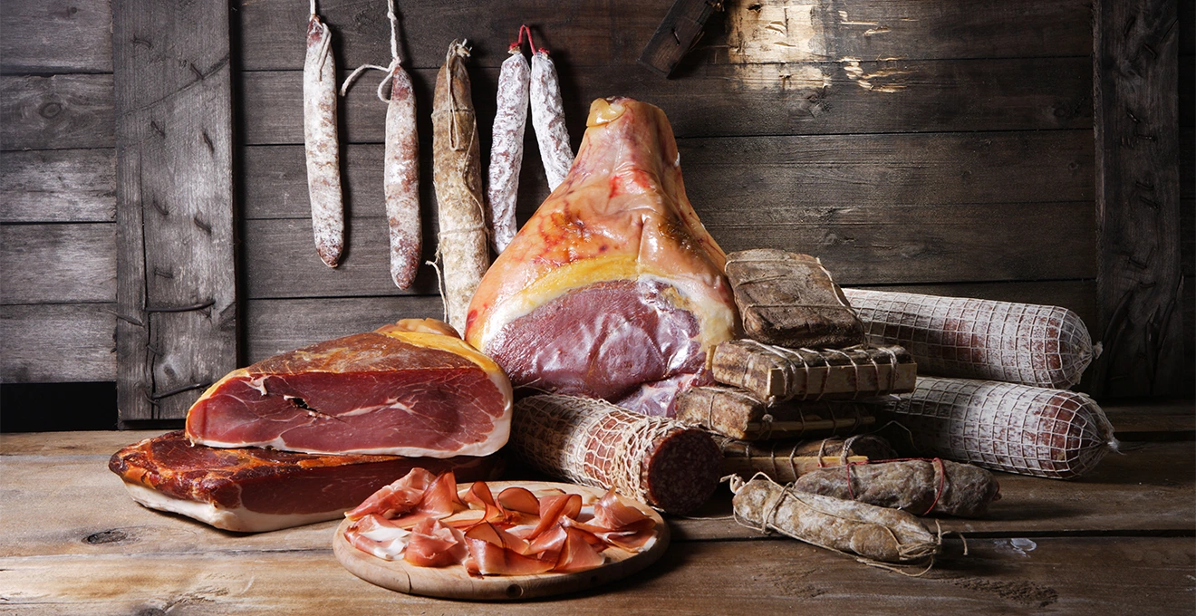Des mains désossent et dénervent une pièce de viande de sanglier avec un couteau à désosser sur une planche en bois.